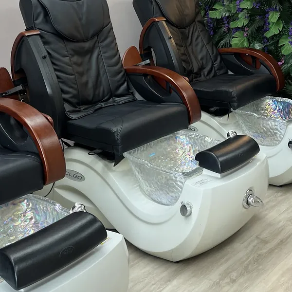 Close view of two black leather massage pedicure chairs with their glass foot basins, beside the green foliage wall